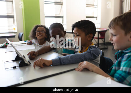 Seitenansicht des Neugierig schoolkids Studieren auf digitalen Tablet beim Sitzen am Schreibtisch im Klassenzimmer der Volksschule Stockfoto