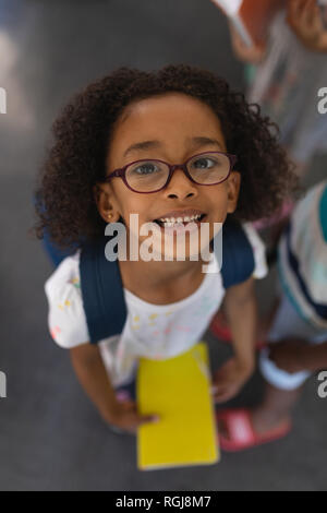 Hohe Betrachtungswinkel der glücklichen Schülerin mit Schultasche an Kamera suchen im Klassenzimmer Stockfoto
