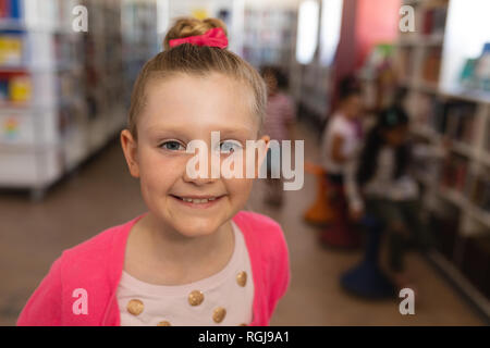 Gerne süßes Schulmädchen auf der Suche ta Kamera in der Schule Bibliothek Stockfoto
