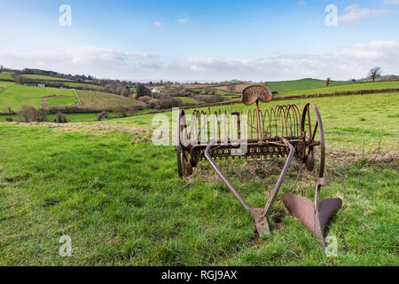Alten rostigen Pferdekutschen Heu rechen in eine Rasenfläche mit Devonshire Landschaft und die Hügel im Hintergrund unter einem blauen und bewölkter Himmel an einem hellen Tag Stockfoto