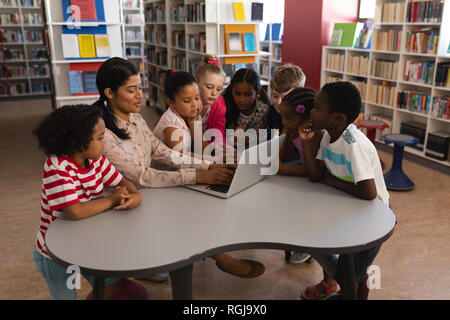 Seitenansicht der weiblichen Lehrer Unterricht neugierig schoolkids auf Laptop am Tisch in der Bibliothek Stockfoto