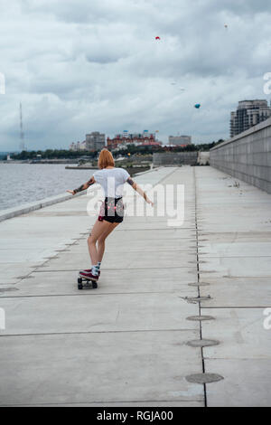 Ansicht der Rückseite des jungen Frau reiten Carver skateboard am Flußufer Stockfoto