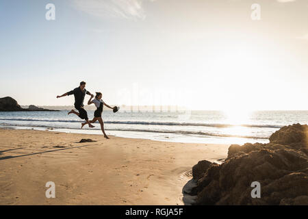 Frankreich, Bretagne, glückliches junges Paar am Strand bei Sonnenuntergang springen Stockfoto