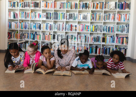 Vorderansicht der weiblichen Lehrer und schoolkids ein Buch lesen Beim liegen auf dem Boden der Schule Bibliothek Stockfoto