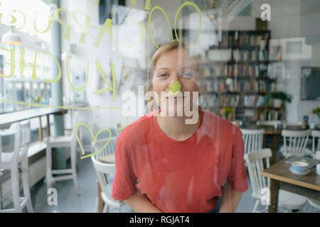 Portrait von lächelnden jungen Frau hinter Fensterglas in einem Cafe posing Stockfoto