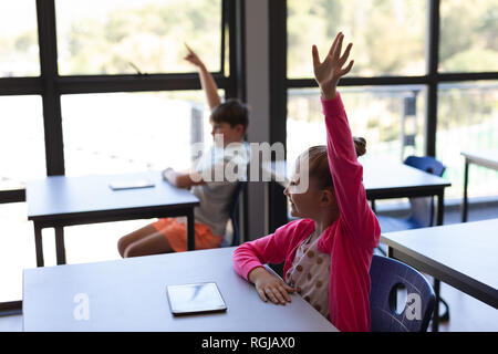 Schule Kinder heben ihre Hand, während er am Schreibtisch im Klassenzimmer sitzen Stockfoto