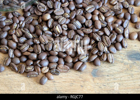 Menge zerstreut geröstete Kaffeebohnen auf einem alten Holztisch Draufsicht Nahaufnahme Stockfoto