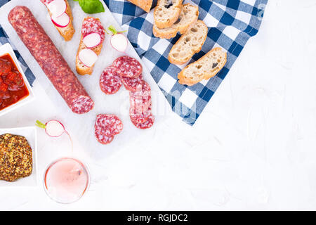 Italienische Salami auf eine weiße Tafel und ein Stein, ein Glas Rose Wein und verschiedene Snacks. Freier Platz für Text. Sandwiches mit Ciabatta und fre Stockfoto
