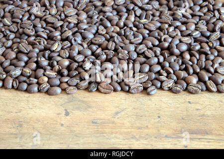 Menge zerstreut geröstete Kaffeebohnen auf einem alten Holztisch Vorderansicht Stockfoto