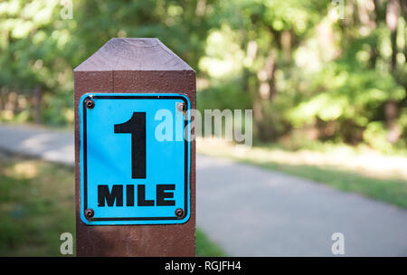 Eine Meile Markierung Schild neben einem asphaltierten Weg mit einem hellen grünen und sonnigen Hintergrund. Stockfoto