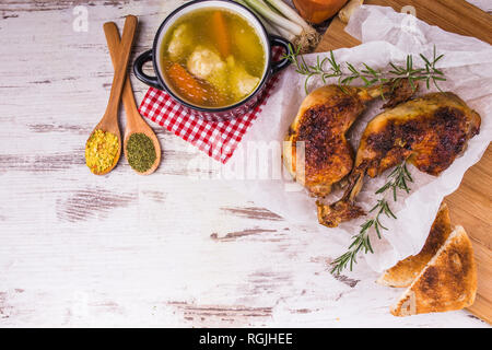 Köstliche Brathähnchen drumstick - Beine mit Rosmarin und Gewürze in Löffel und Hühnersuppe serviert in einem traditionellen Schüssel auf einem rustikalen Holzmöbeln backgroun Stockfoto