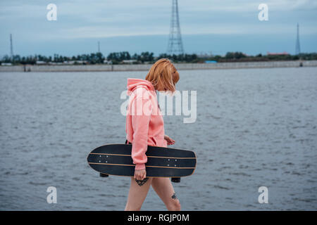 Junge Frau mit Carver skateboard Wandern am Flußufer Stockfoto