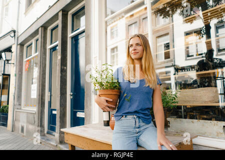 Niederlande, Maastricht, blonde junge Frau mit Blumentopf in der Stadt Stockfoto