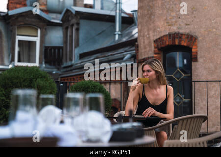 Junge Frau sitzt auf der Dachterrasse trinken Tasse Kaffee Stockfoto