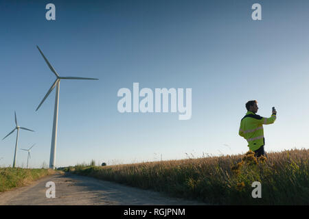 Ingenieur steht ein Feld an einem Wind mittels Handy Farm Stockfoto