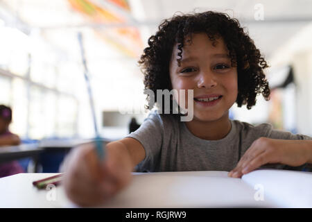 Glückliche Schüler an Kamera am Schreibtisch im Klassenzimmer auf der Suche Stockfoto