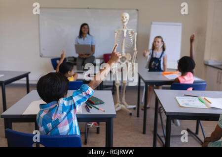 Ansicht der Rückseite des schoolkids heben die Hände am Schreibtisch im Klassenzimmer der Volksschule Stockfoto