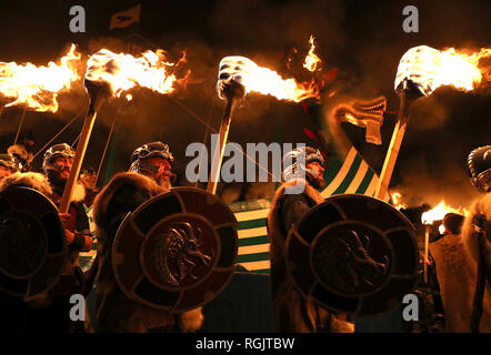 Mitglieder der Jarl Squad März neben der Küche, wie sie durch die lerwick vor der Kombüse auf Feuer auf den Shetland Inseln während der Up Helly Aa Wikinger Fest gesetzt wird. Mit Ursprung in den 1880er Jahren, das Festival feiert den Shetland nordischen Erbe. Stockfoto