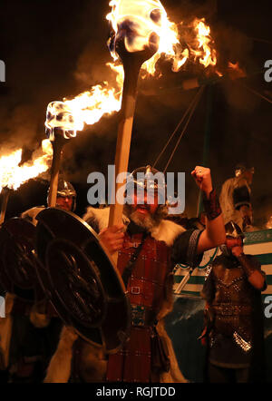 Mitglieder der Jarl Squad März neben der Küche, wie sie durch die lerwick vor der Kombüse auf Feuer auf den Shetland Inseln während der Up Helly Aa Wikinger Fest gesetzt wird. Mit Ursprung in den 1880er Jahren, das Festival feiert den Shetland nordischen Erbe. Stockfoto