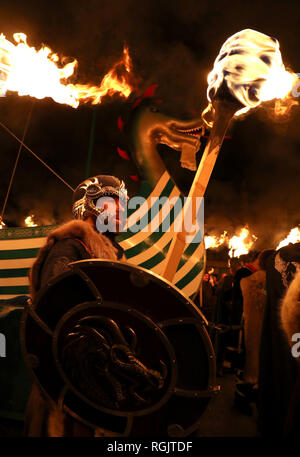 Mitglieder der Jarl Squad März neben der Küche, wie sie durch die lerwick vor der Kombüse auf Feuer auf den Shetland Inseln während der Up Helly Aa Wikinger Fest gesetzt wird. Mit Ursprung in den 1880er Jahren, das Festival feiert den Shetland nordischen Erbe. Stockfoto