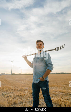 Portrait von lächelnden jungen Mann mit der Mistgabel auf Stoppeln Feld Stockfoto