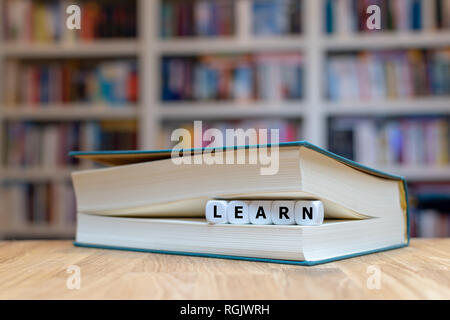 Würfel in Buchform das Wort "Lernen". Buch liegt auf einem hölzernen Tisch in einer Bibliothek. Stockfoto