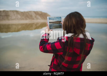 Junge Frau mit Foto mit Tablette am Strand Stockfoto