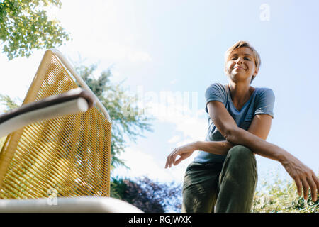 Portrait von lächelnden Frau im Garten neben Stuhl Stockfoto