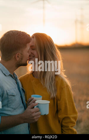 Glückliches junges Paar hält Becher in ländlichen Landschaft küssen Stockfoto