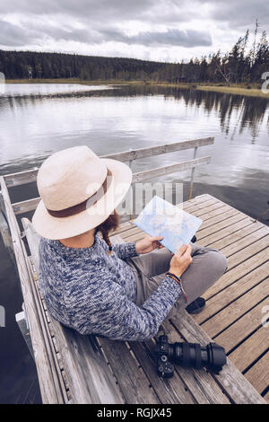 Schweden, Lappland, Mann mit Kamera sitzt auf der Bank an der Mole in Karte suchen Stockfoto