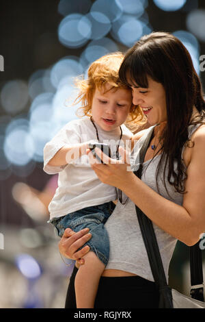 Junge Frau etwas Übersicht zu ihren jungen Sohn auf ein Handy. Stockfoto