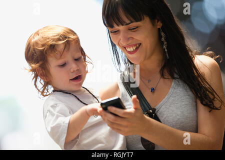 Junge Frau etwas Übersicht zu ihren jungen Sohn auf ein Handy. Stockfoto