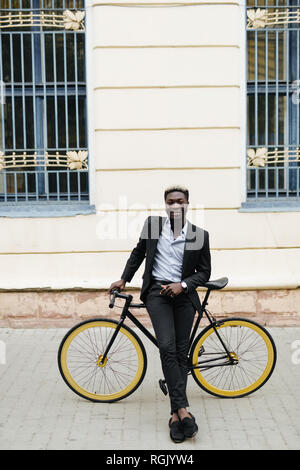 Schönen afrikanischen Mann, den ich auf der Straße mit dem Fahrrad. Afrikanischer Mann in casuals Walking im Freien in der Stadt mit dem Fahrrad. Stockfoto