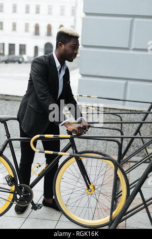 Jungen schönen afrikanischen Mann in Anzug Parkplatz sein Fahrrad auf der Straße Stockfoto