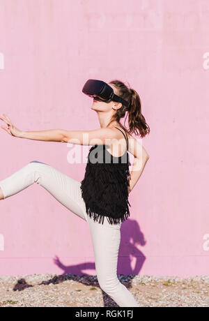 Junge Frau mit VR-Brille vor rosa Wand Stockfoto