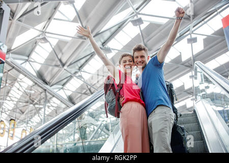 Glückliches Paar jubelnd auf Rolltreppe am Flughafen Stockfoto