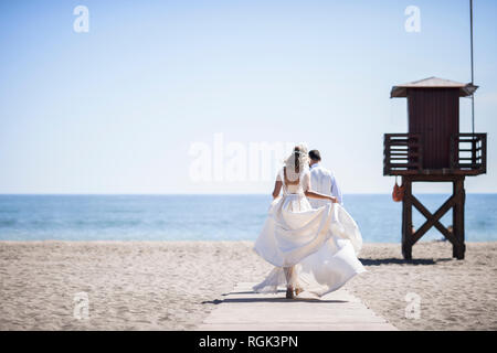 Rückansicht des Brautpaar genießen Hochzeitstag zu Fuß am Strand Stockfoto
