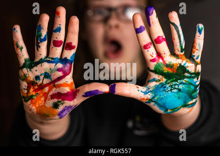 Ein Kind glücklich oder überrascht, als ihre Hände sind in Rot, Rosa, Gelb, Orange, Rot, Blau, Grün und lila Tinte. Konzepte: Kunst, Kreativität Stockfoto