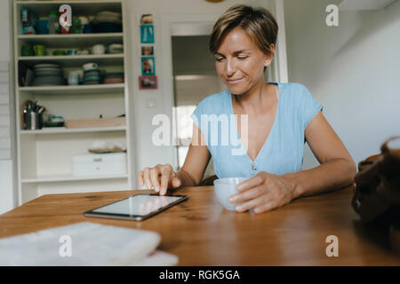 Frau sitzt am Tisch zu Hause bei einer Tasse Kaffee und Tablet Stockfoto