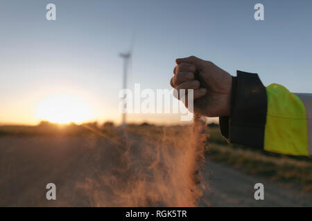 Nahaufnahme der Hand des Menschen Streuung Boden bei Windenergieanlagen bei Sonnenuntergang Stockfoto