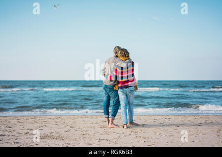 Ture Paar stehend auf den Strand mit den Armen herum, mit Blick auf das Meer Stockfoto