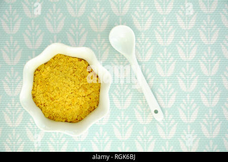 Nährhefe Flocken in die kannelierten weißen Schüssel und Löffel auf hellem Türkis strukturierten Hintergrund Schuß von oben. Horizontales Format mit Platz für Text. Stockfoto