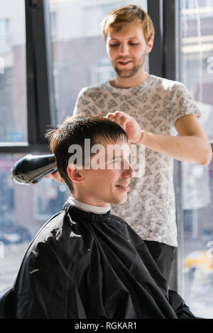 Friseur mit Haartrockner trocknen und stylen von Client. Styling Konzept Stockfoto