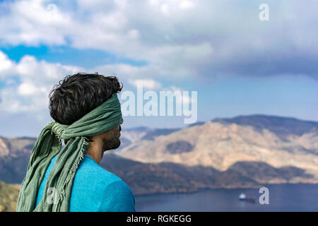 Junger Mann mit blindfolder auf Augen auf der Spitze einer Klippe über Meer und Landschaft