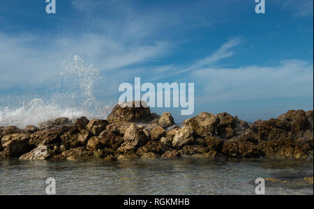 Schönen karibischen Strand Szene als Wellen beginnen über die Mauer zum Schutz eines klaren, warmen Meer Gezeiten Pool zum Absturz zu bringen. Dramatische Wellen mit hellen Himmel. Stockfoto