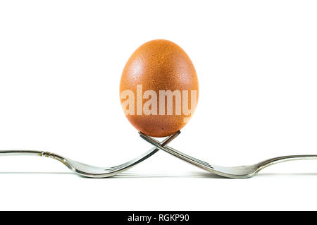 Eine braune organische Ei auf zwei Gabeln auf weißem Hintergrund isoliert ausgeglichen. Stockfoto