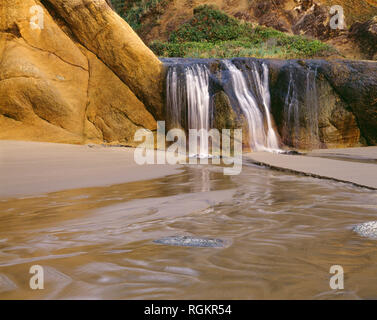 USA, Oregon, Hug Point State Park, Wasserfall auf der Fall Creek stolpert über bunten Sandsteinfelsen. Stockfoto