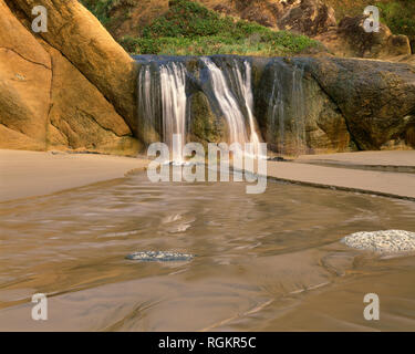 USA, Oregon, Hug Point State Park, Wasserfall auf der Fall Creek stolpert über bunten Sandsteinfelsen. Stockfoto