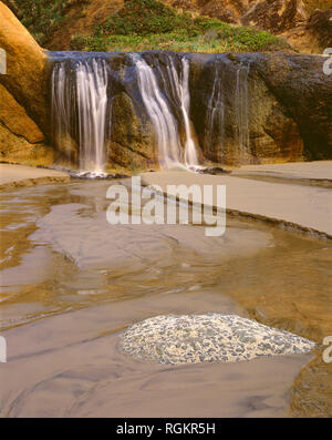 USA, Oregon, Hug Point State Park, Wasserfall auf der Fall Creek stolpert über bunten Sandsteinfelsen. Stockfoto