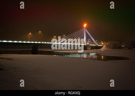 Jätkänkynttilä Schrägseilbrücke über den Eisbedeckten Fluss Kemijoki in der Nacht beleuchtung mit kleinen Spuren der Nordlichter am Himmel. Stockfoto